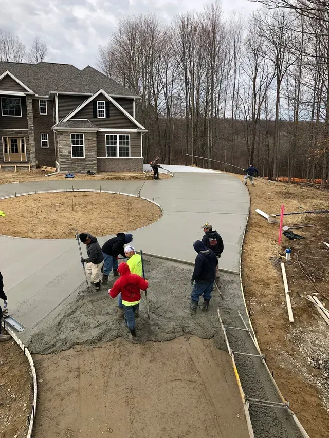 A group of people are working on a concrete driveway in front of a house.