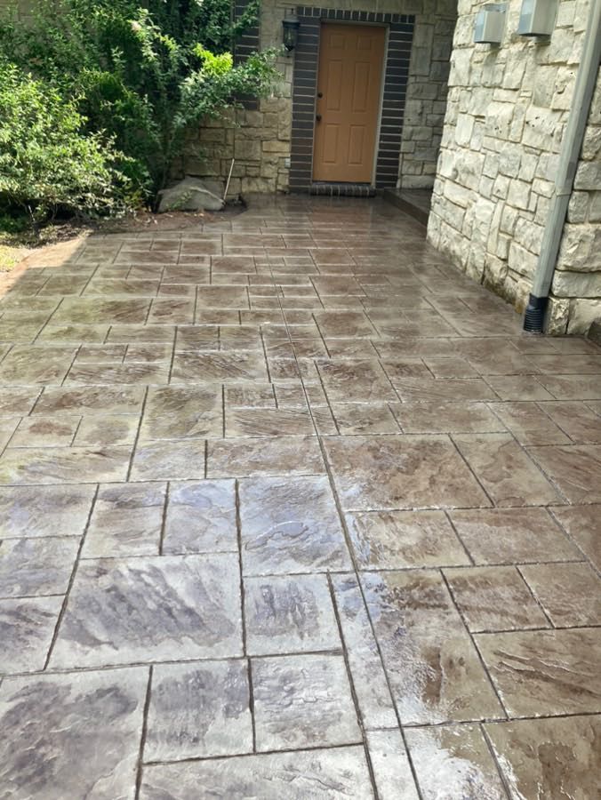 A concrete walkway in front of a stone building with a door.