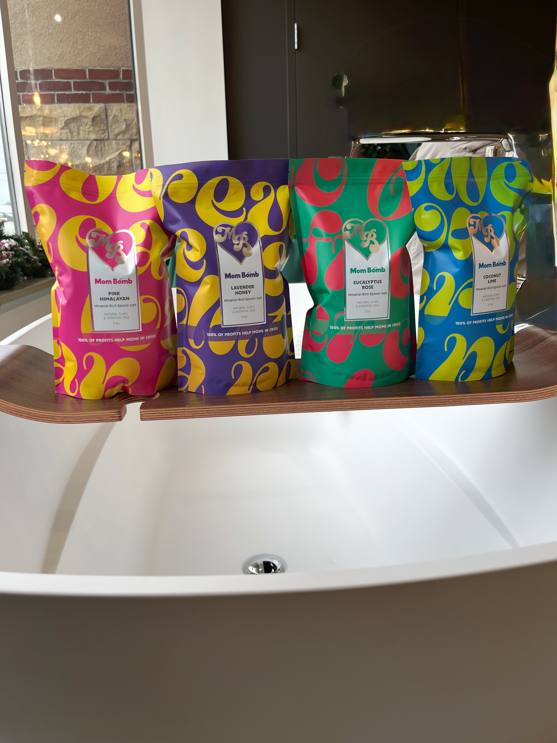 Four colorful bath products on a wooden tray over a white bathtub.