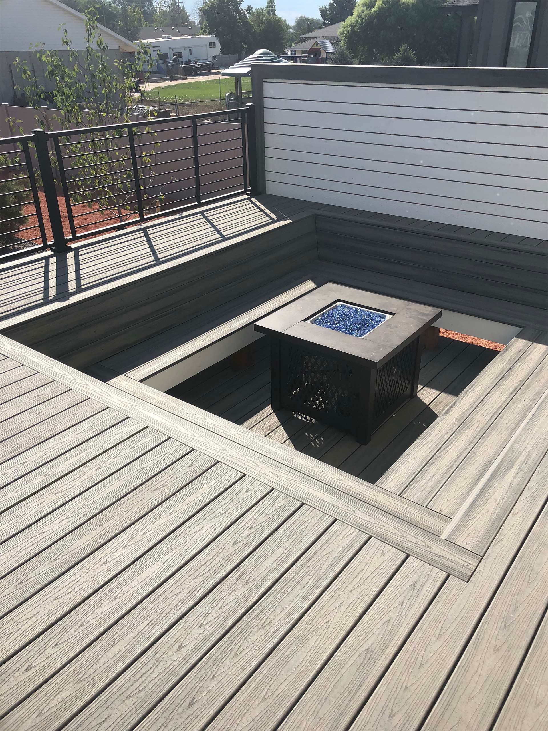Raised deck with a built-in fire pit. Gray composite decking, black railing, and a white privacy screen.