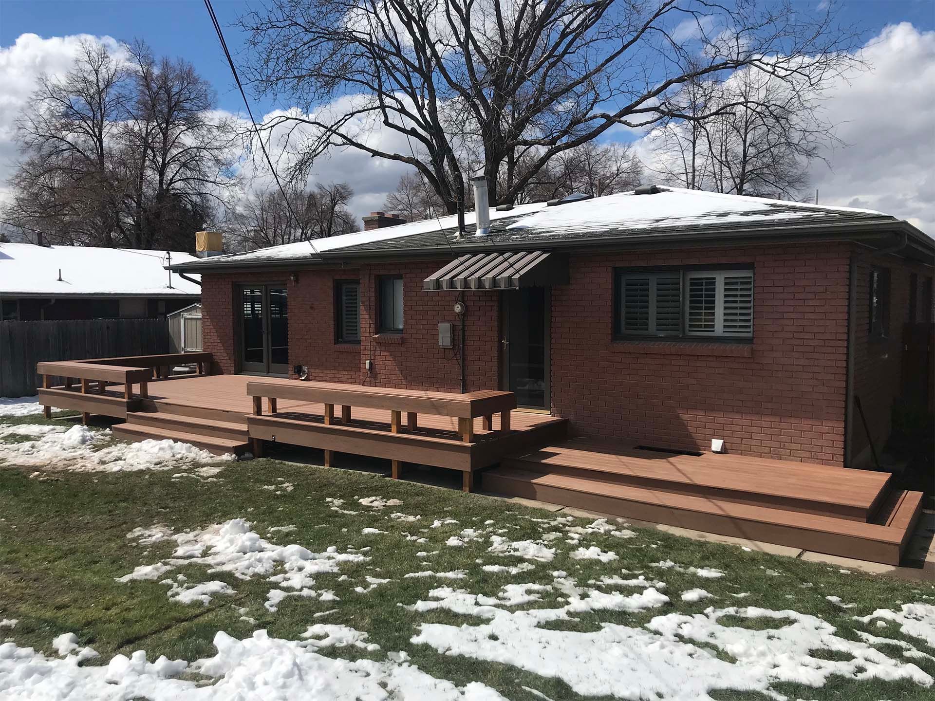 Brick house with a large wooden deck covered in patches of snow.