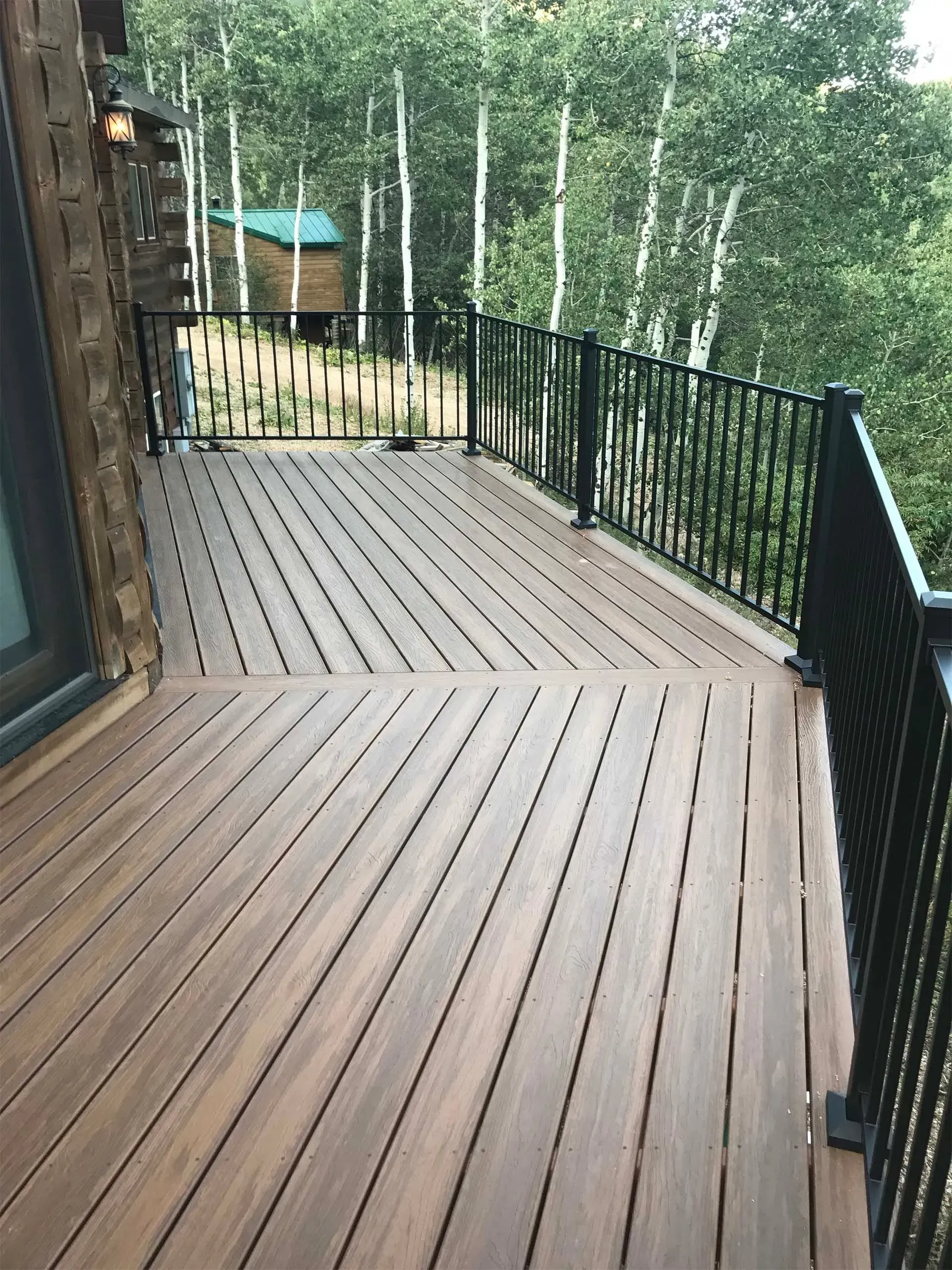 Wooden deck with black railing overlooking a forest and a small treehouse.