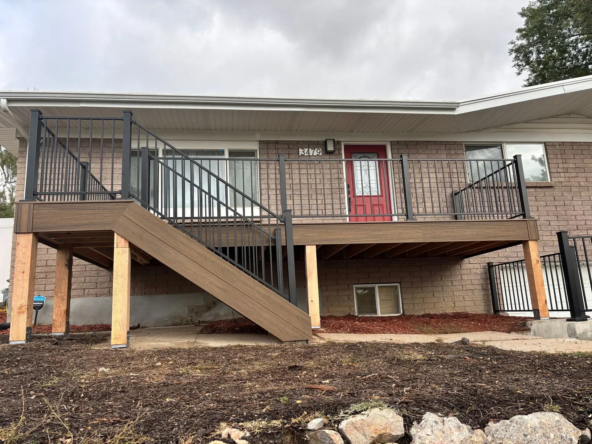 Brown deck with black railing, stairs, and a red door on a brick house.