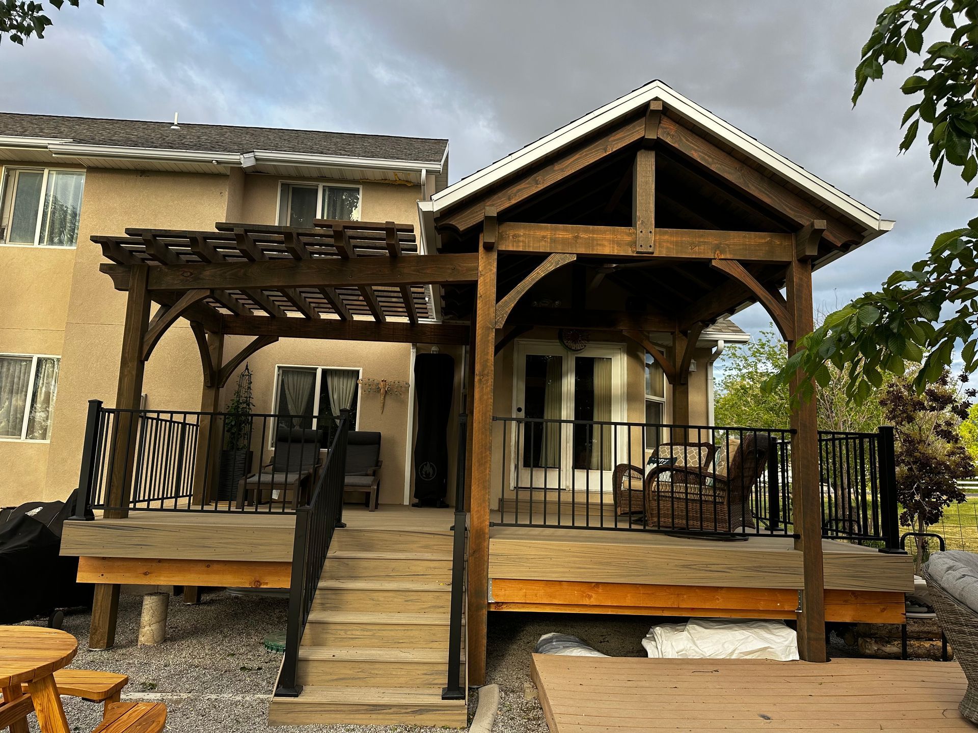 Wooden deck with pergola and covered sitting area attached to a two-story house.