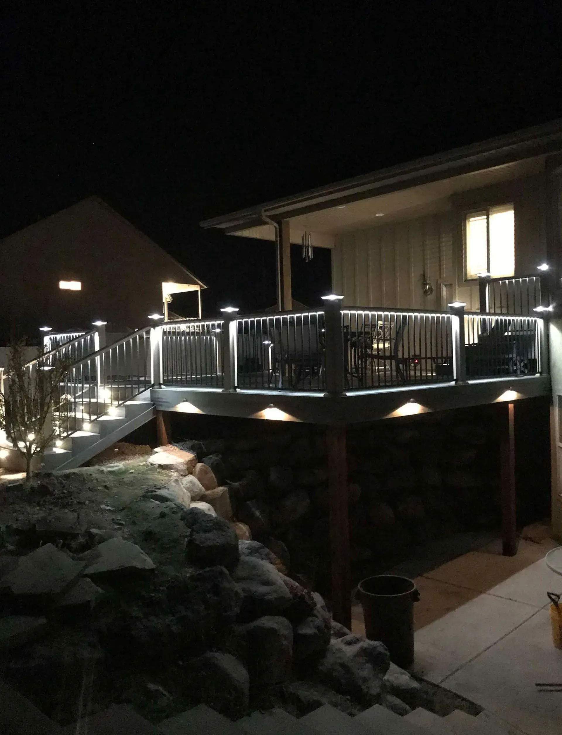 Lit-up deck at night with built-in lights on railings and steps. House in background, rocky landscape in foreground.