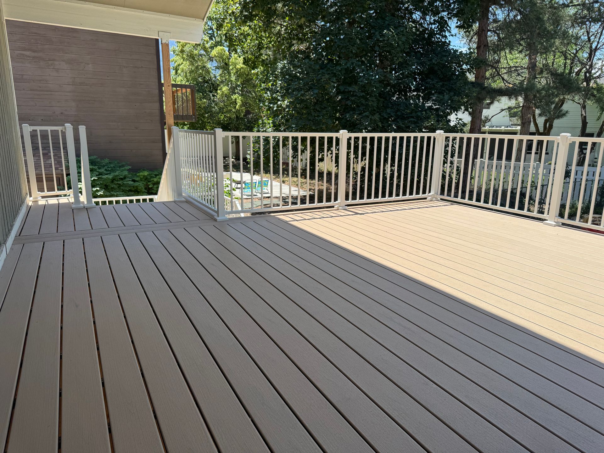 Wooden deck with white railing, overlooking a backyard with trees and a pool.
