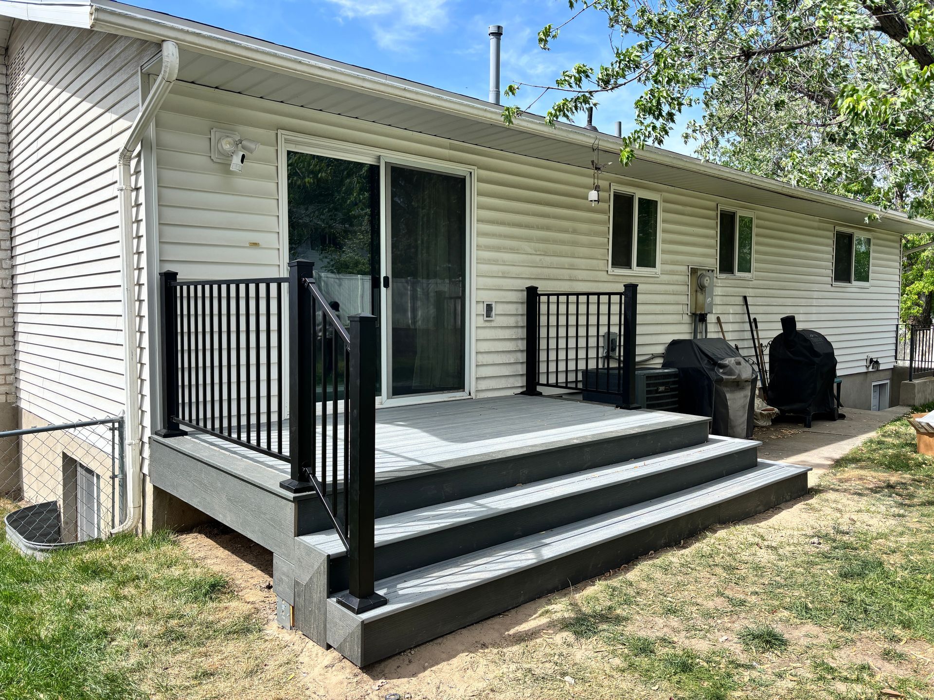 A backyard deck with black railings and gray steps, leading to a sliding glass door.