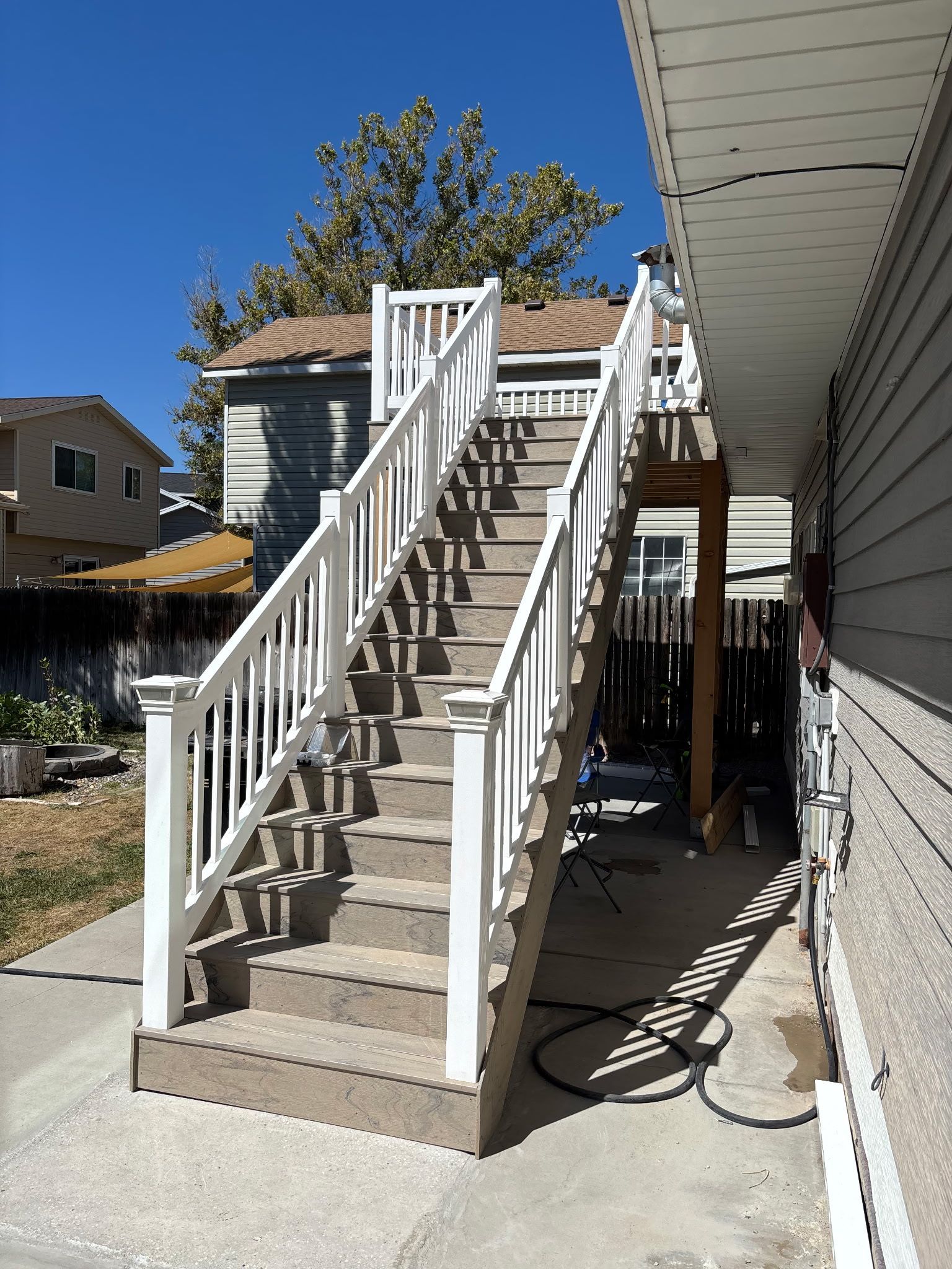 Outdoor staircase with white railings and gray steps leading to a wooden platform. Sunny day.