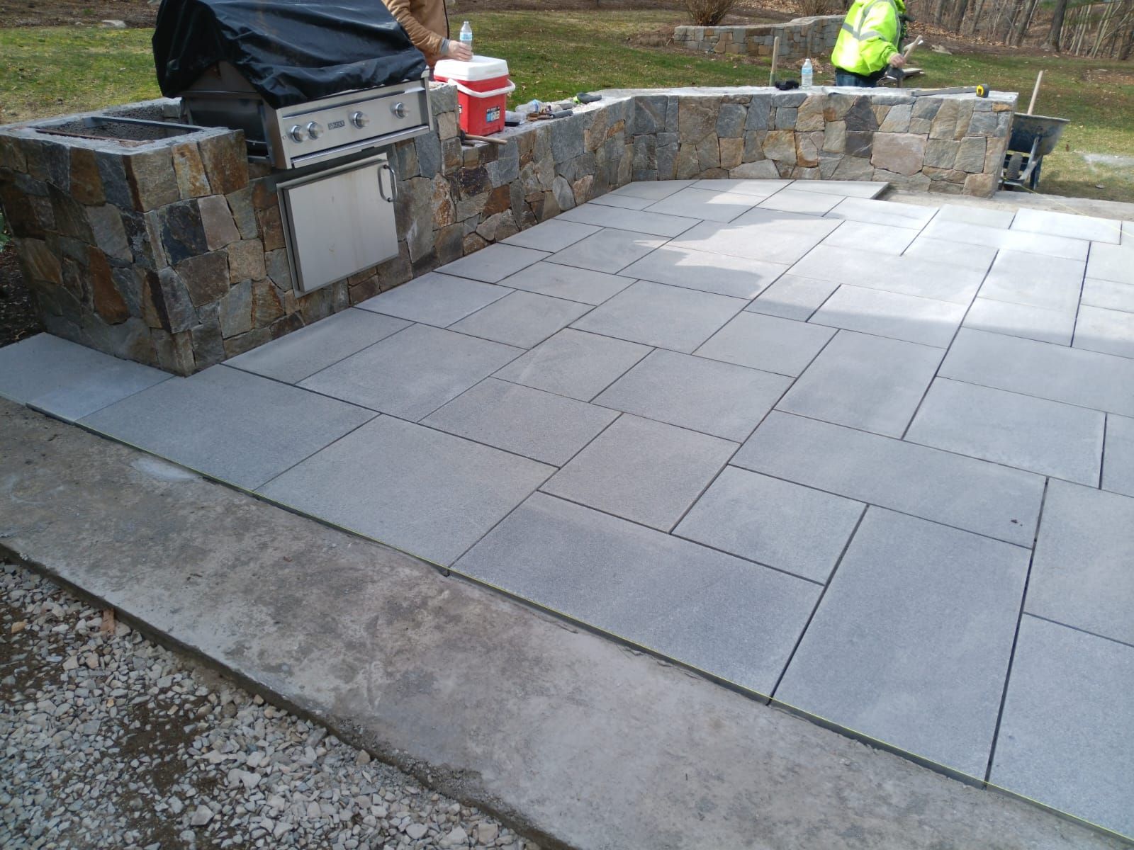 A man is working on a patio with a grill in the background.