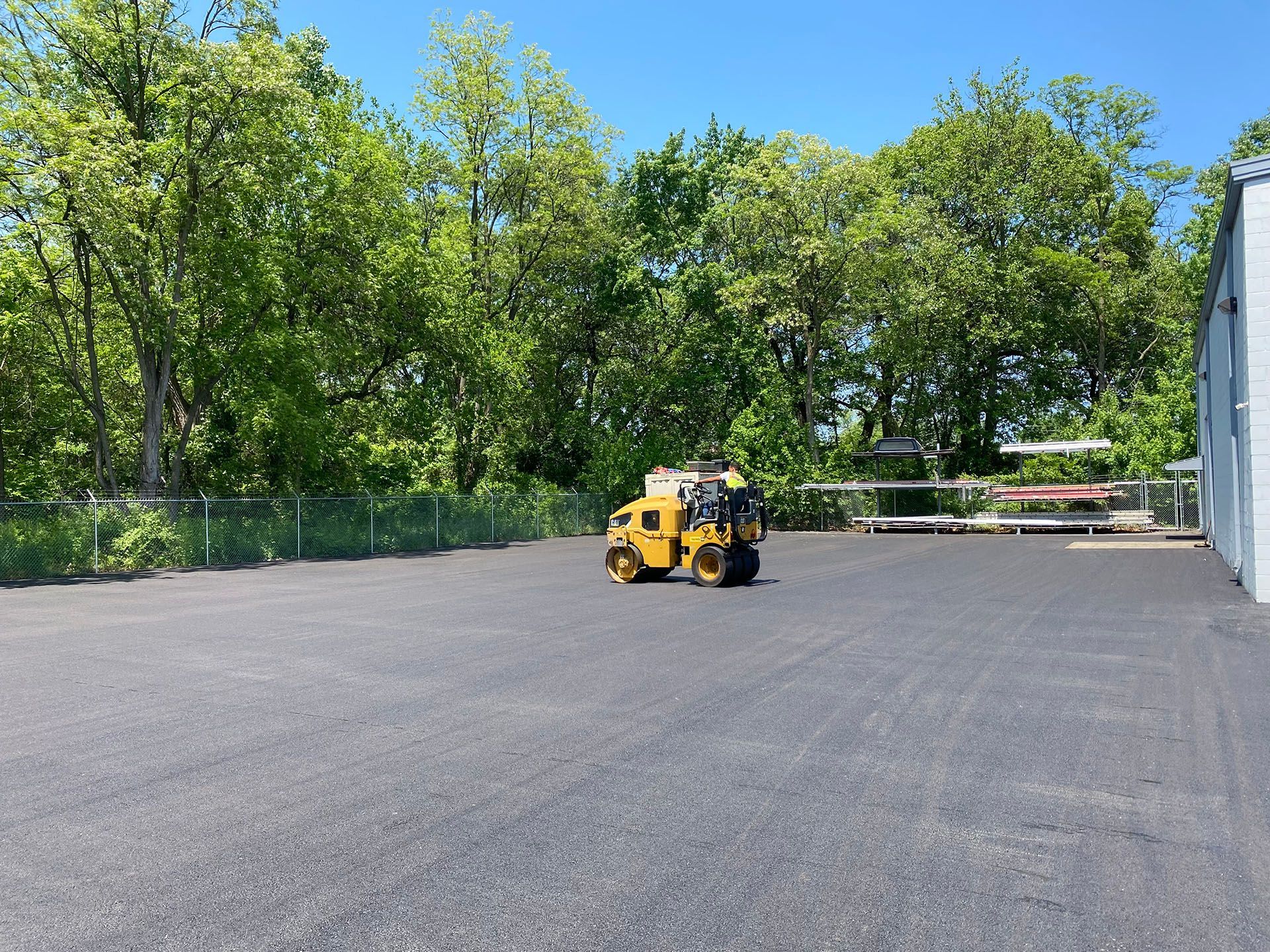 A yellow roller is rolling asphalt in a parking lot.