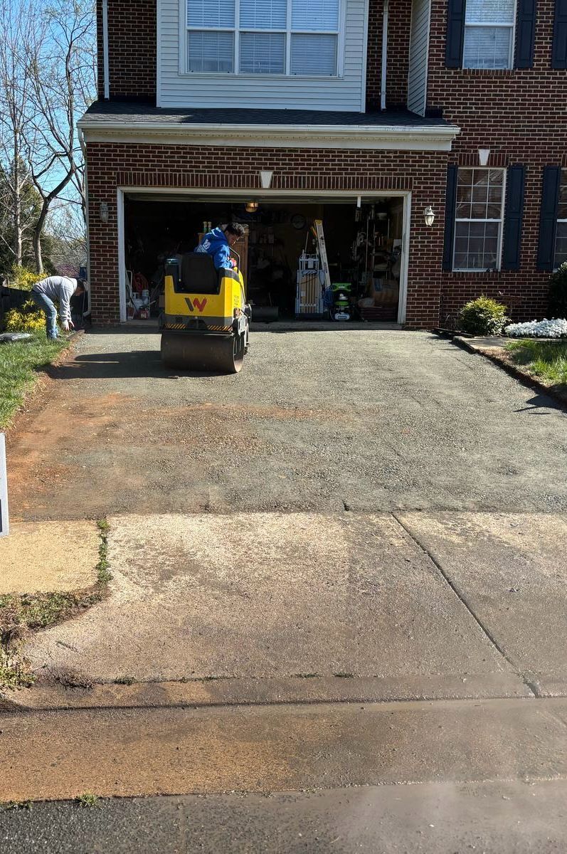 A yellow roller is driving down a driveway in front of a brick house.