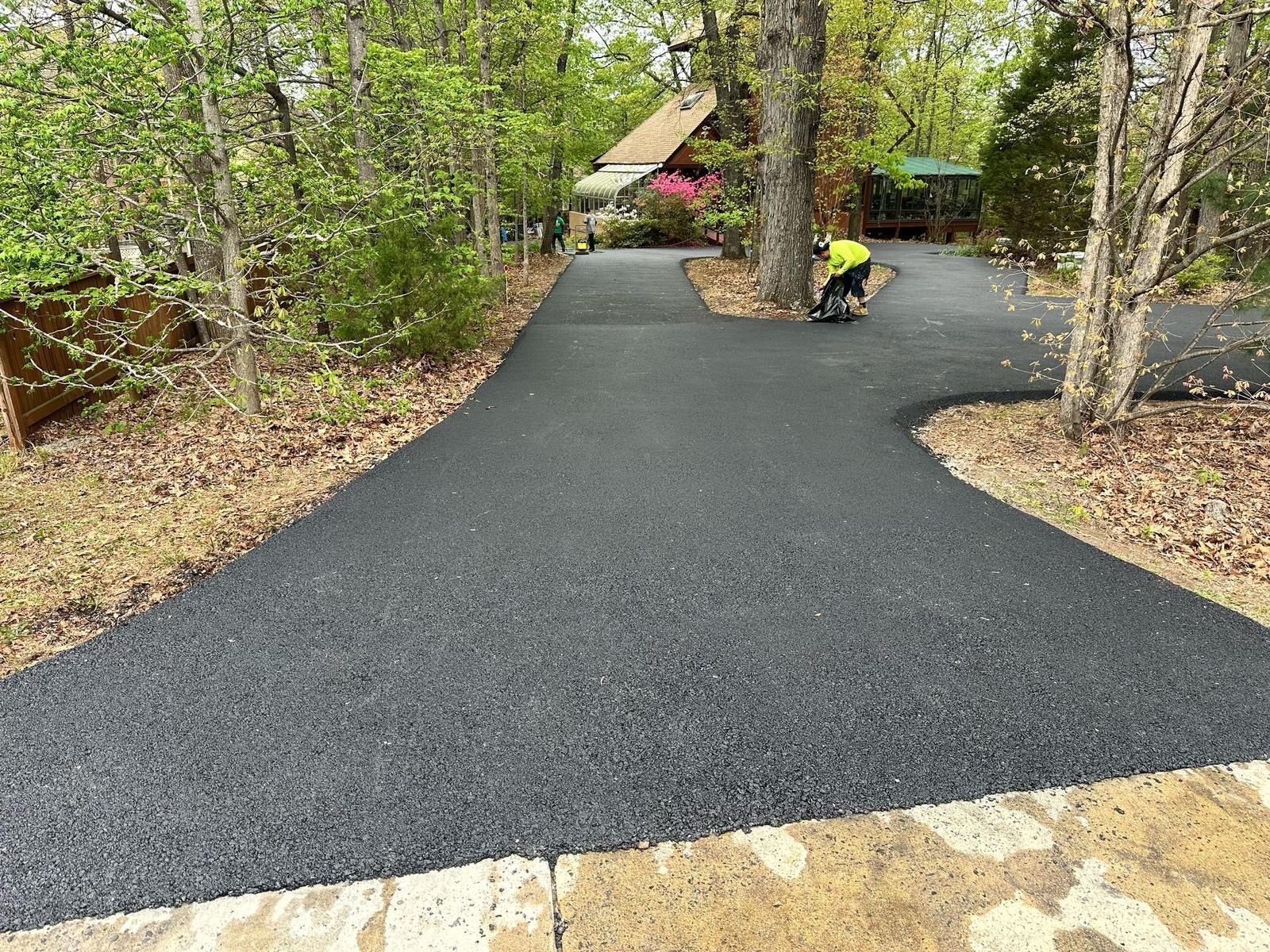 A man is laying asphalt on a driveway in the woods.