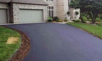 A man is laying asphalt on a driveway in the woods.