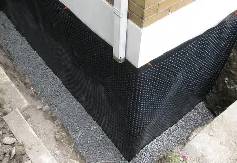 A corner of a house with a black drainage mat on it