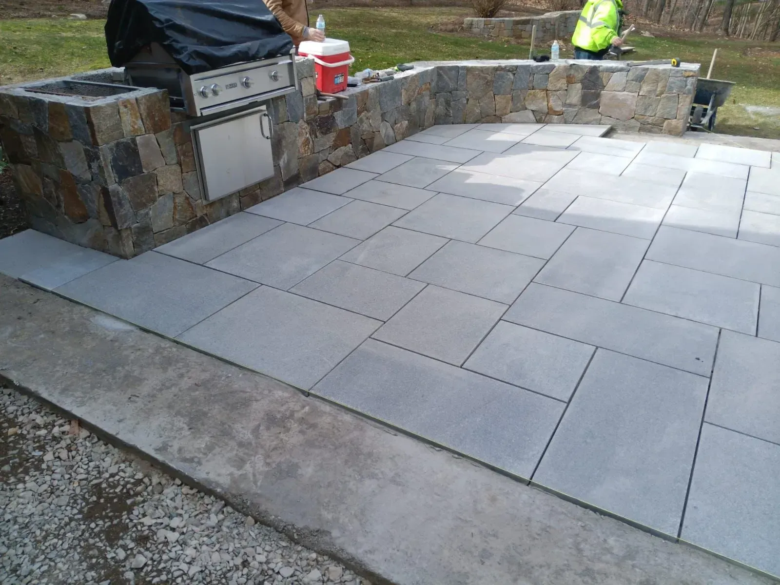 A man is working on a patio with tiles and a grill.