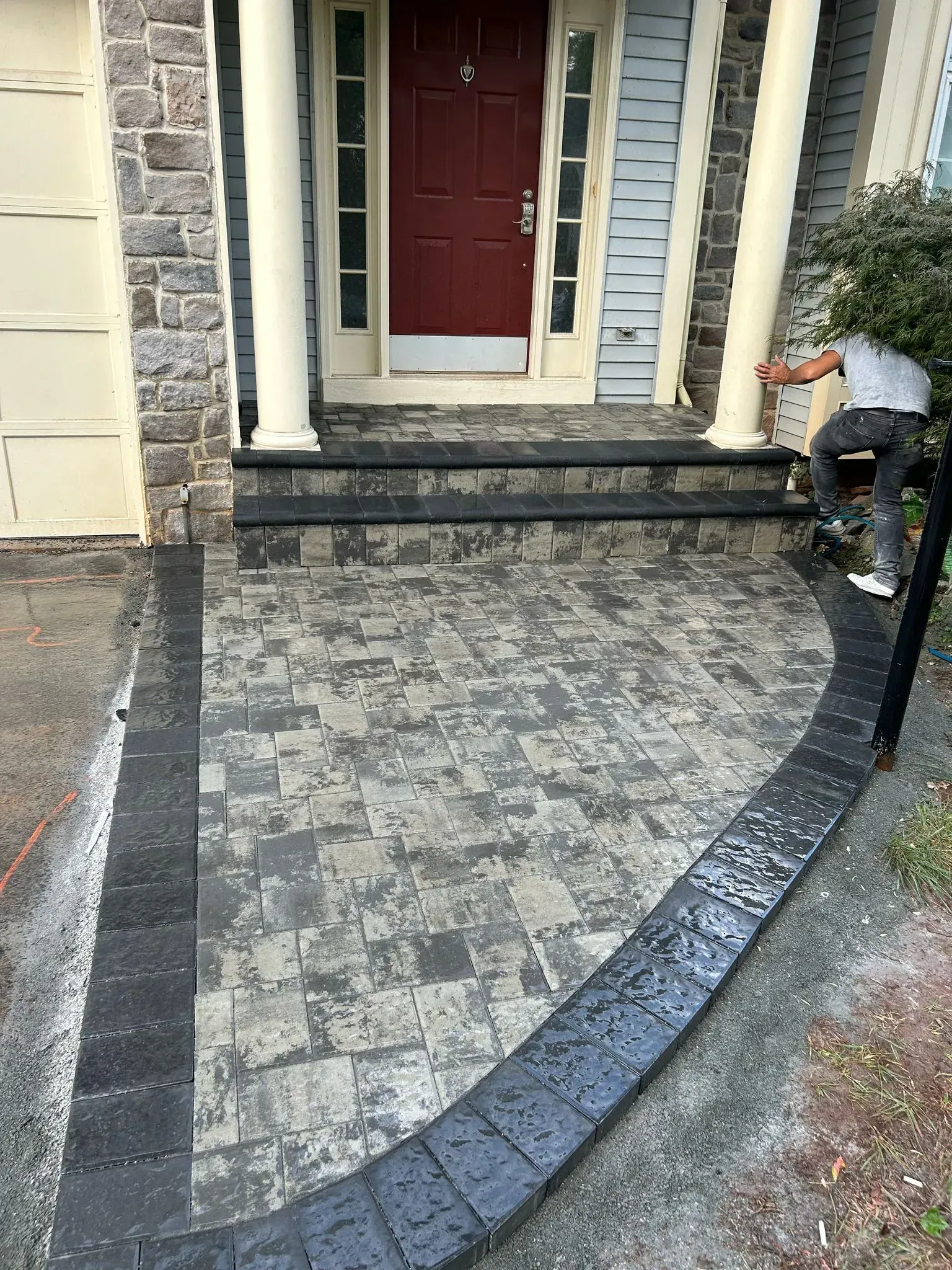 A man is painting a brick walkway in front of a house.
