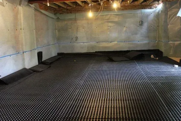 An empty basement with a drainage mat on the floor.