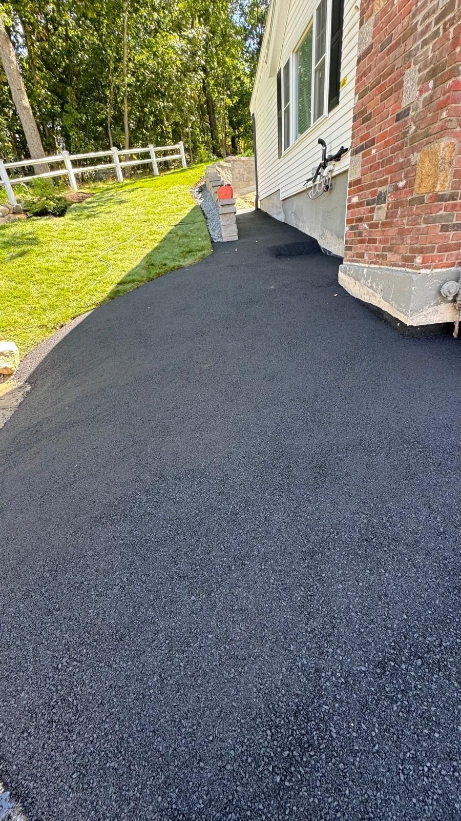 A black asphalt driveway next to a brick house.