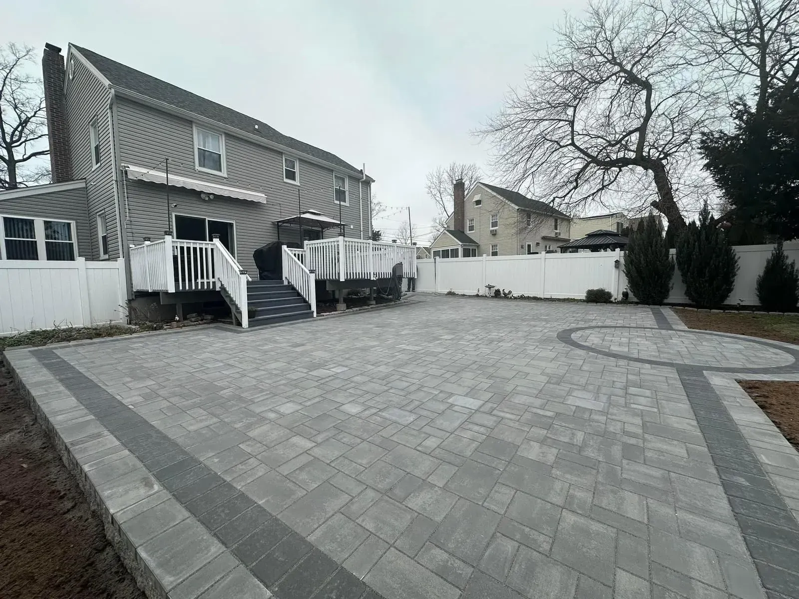A large brick driveway with a deck in the backyard of a house.