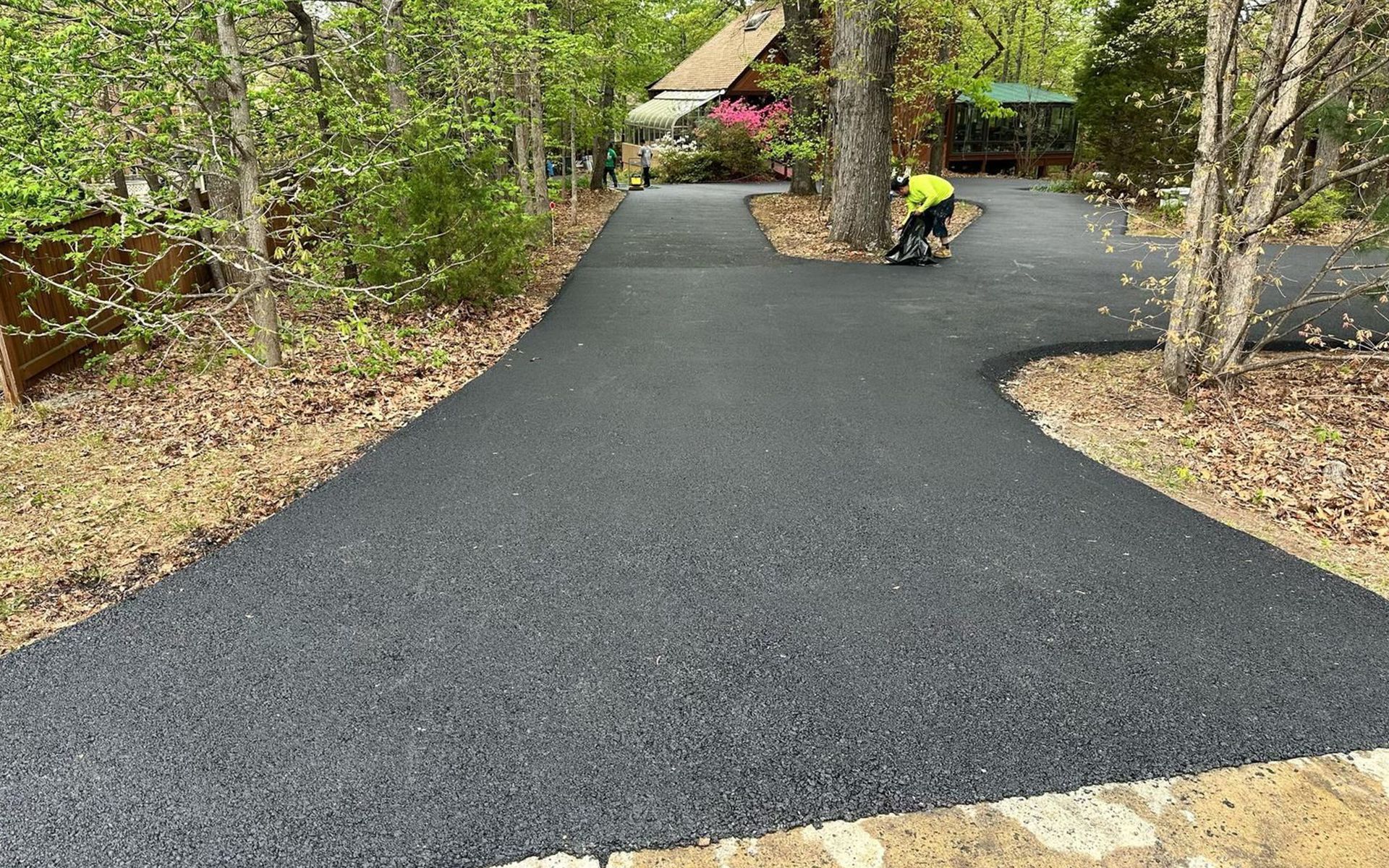 A man is laying asphalt on a driveway in the woods.