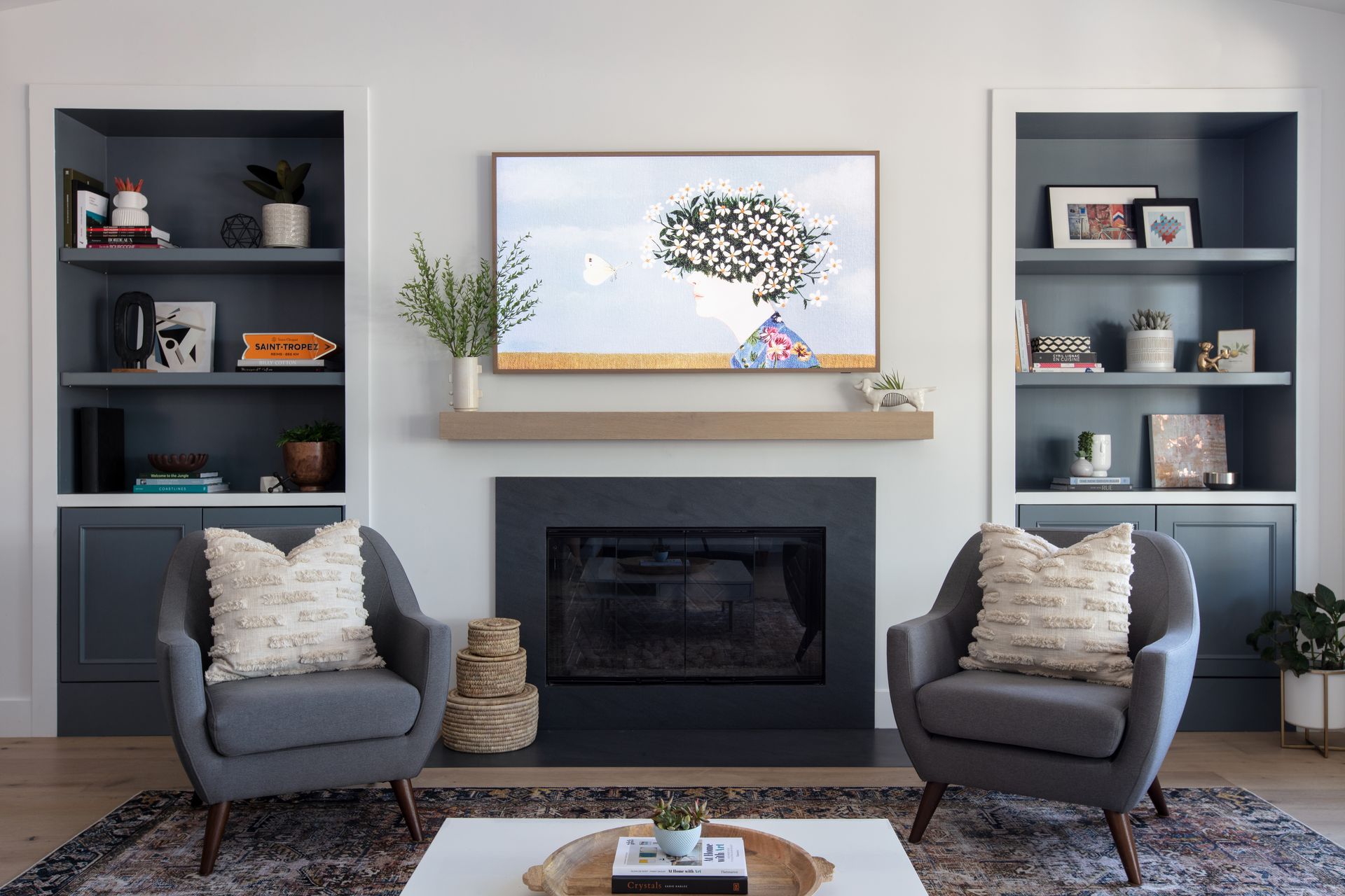 Modern living room with fireplace, two gray chairs, built-in shelves, and a mounted TV above the mantel