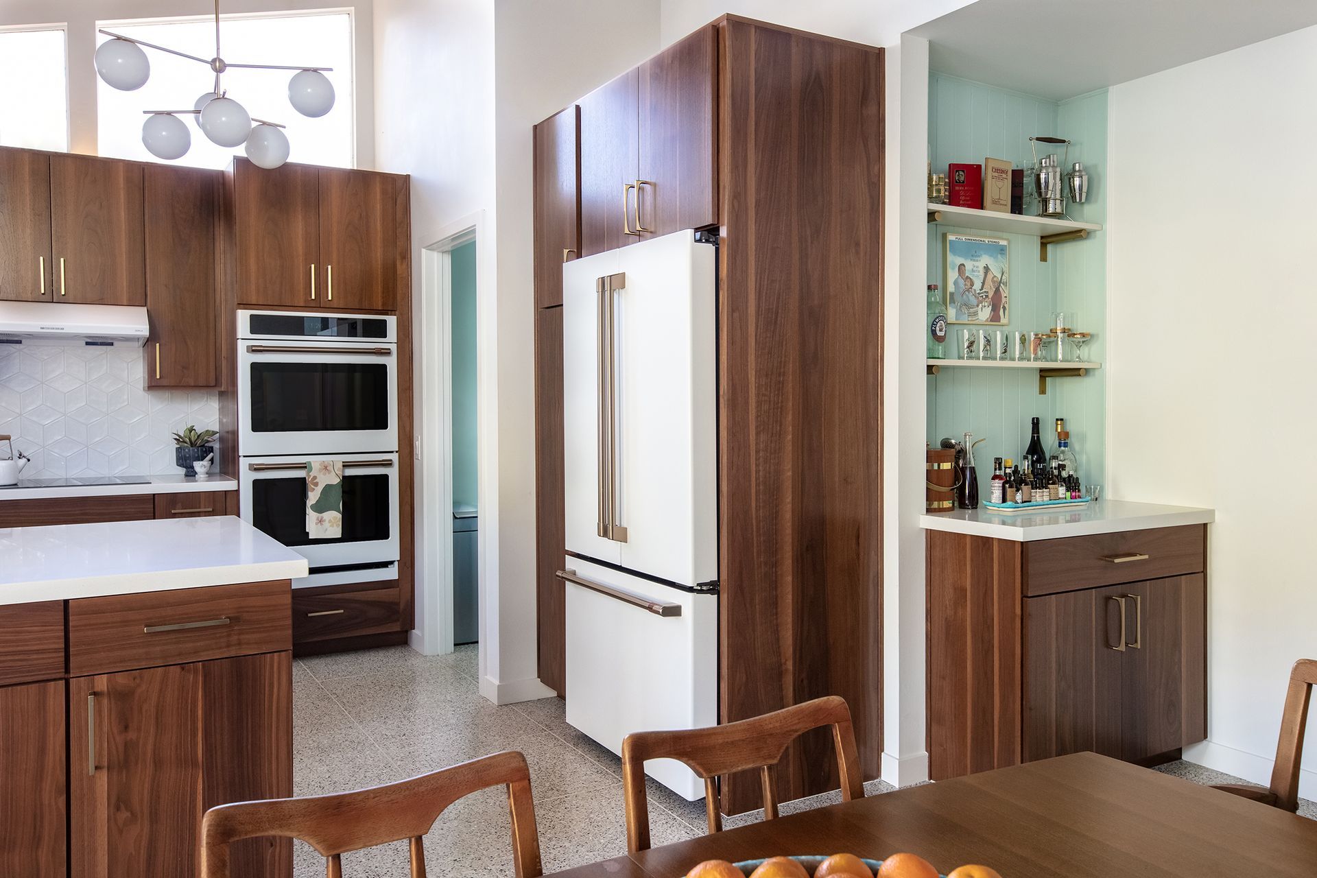 Modern kitchen with wood cabinets, white appliances, and a dining table in the foreground.