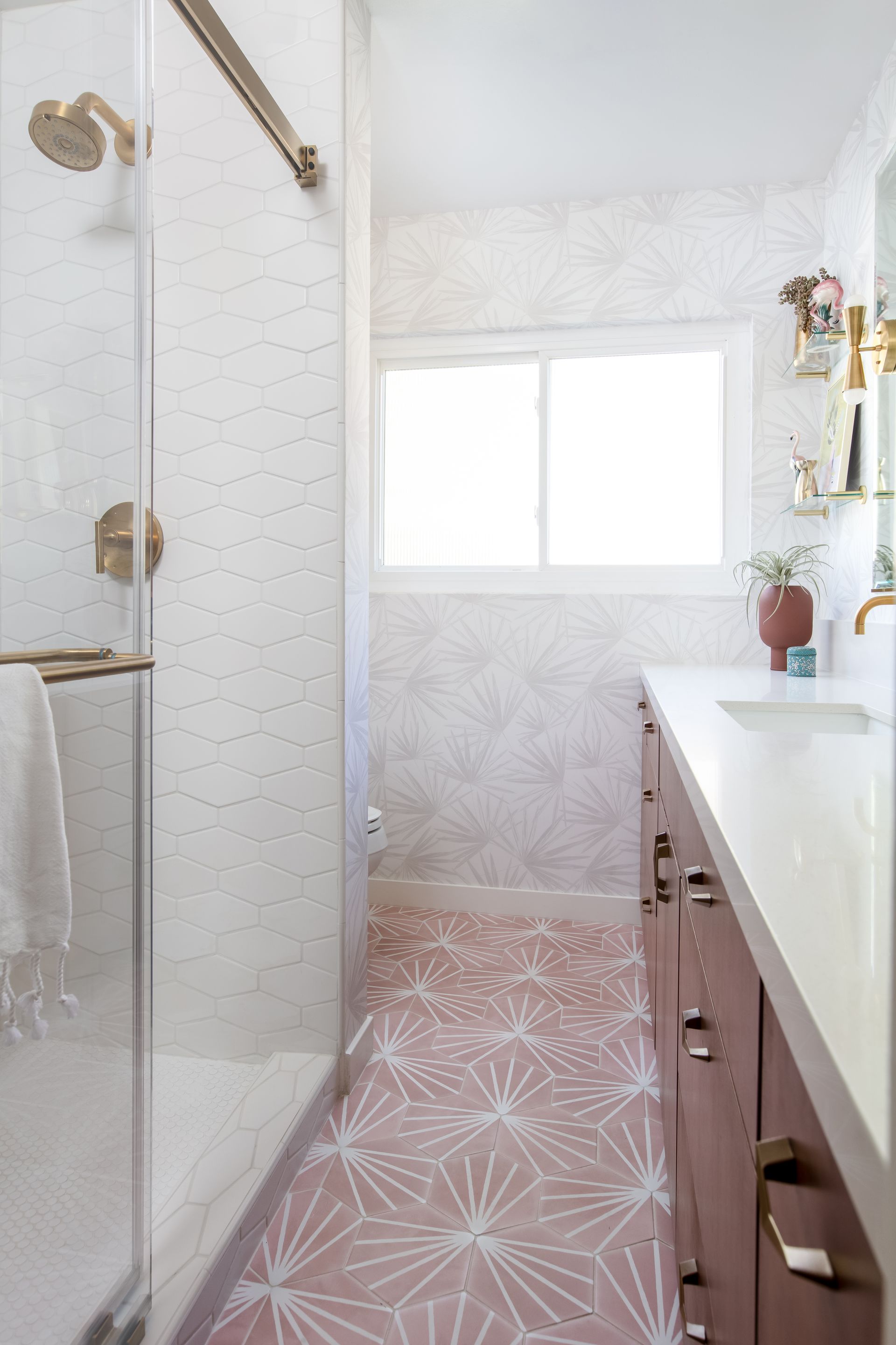 Narrow bathroom with glass shower, pink patterned floor, white vanity, and frosted window.