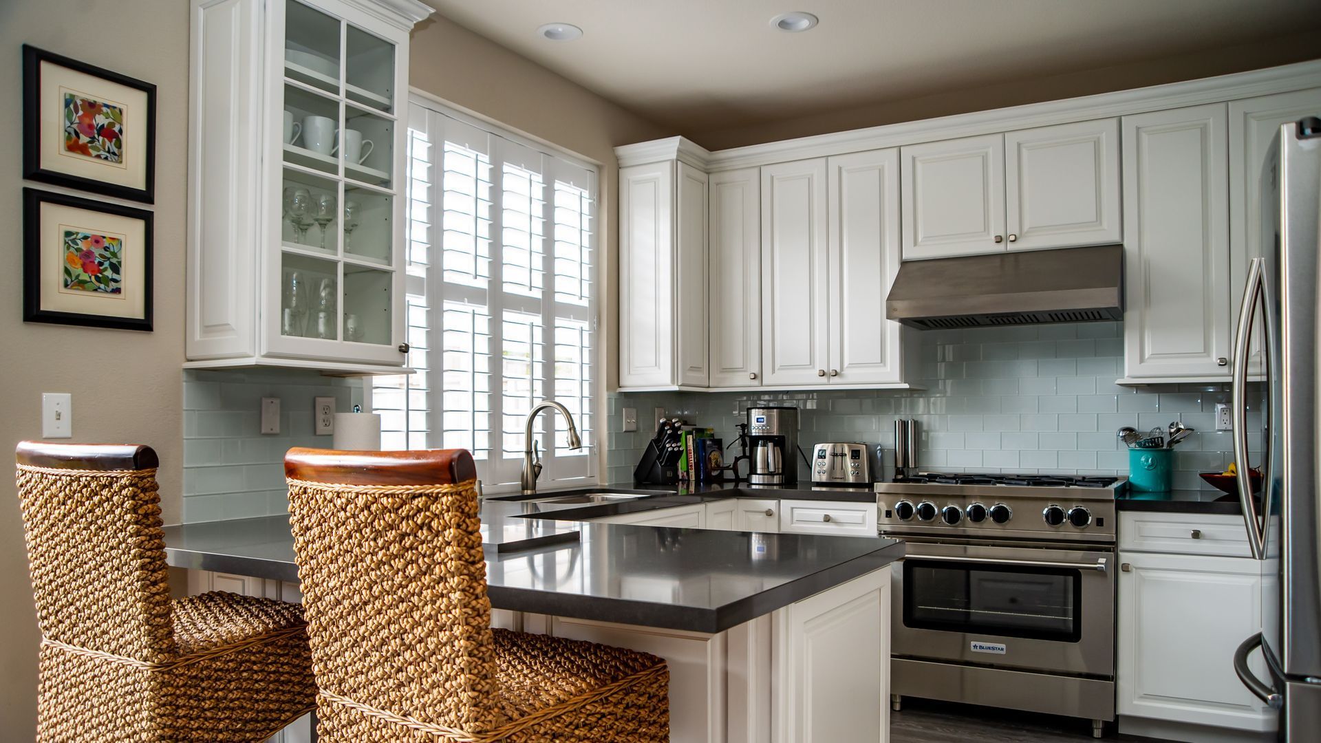 Bright modern kitchen with white cabinets, stainless steel stove, island, and wicker chairs by a window
