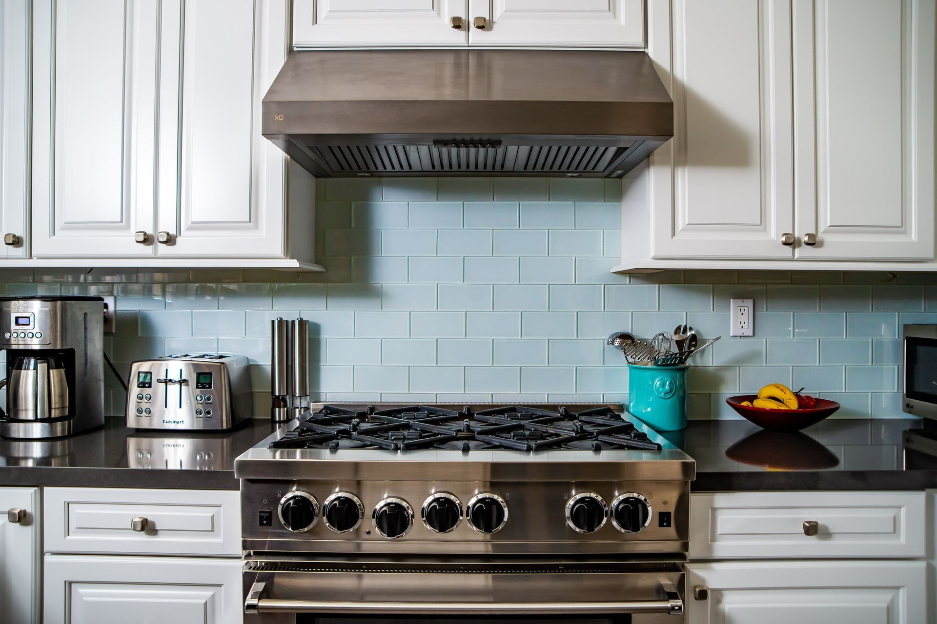 Modern kitchen with stainless steel stove, light blue tile backsplash, white cabinets, and countertop appliances