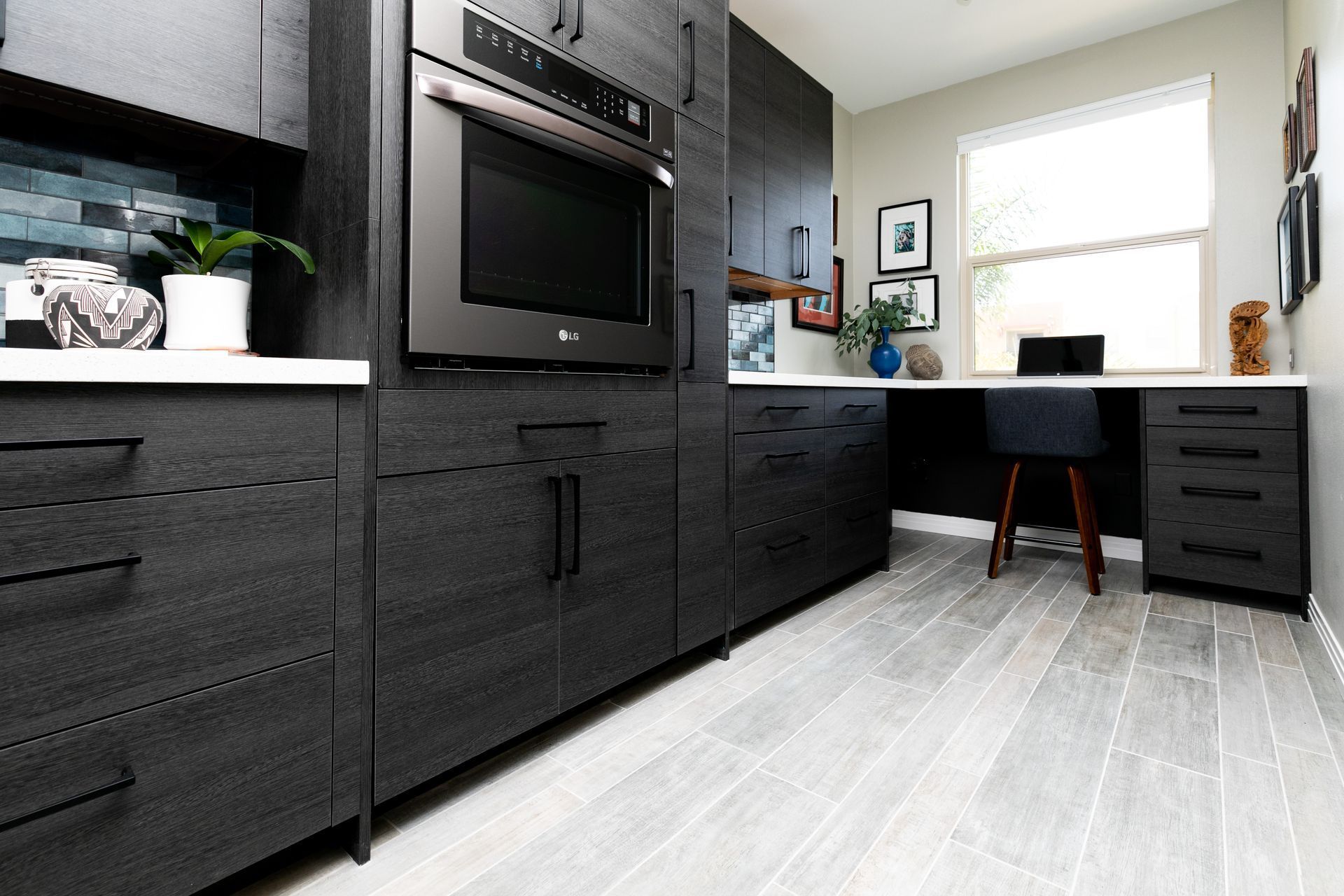Modern kitchen with dark cabinets, white countertop, built-in oven, and bright window desk area