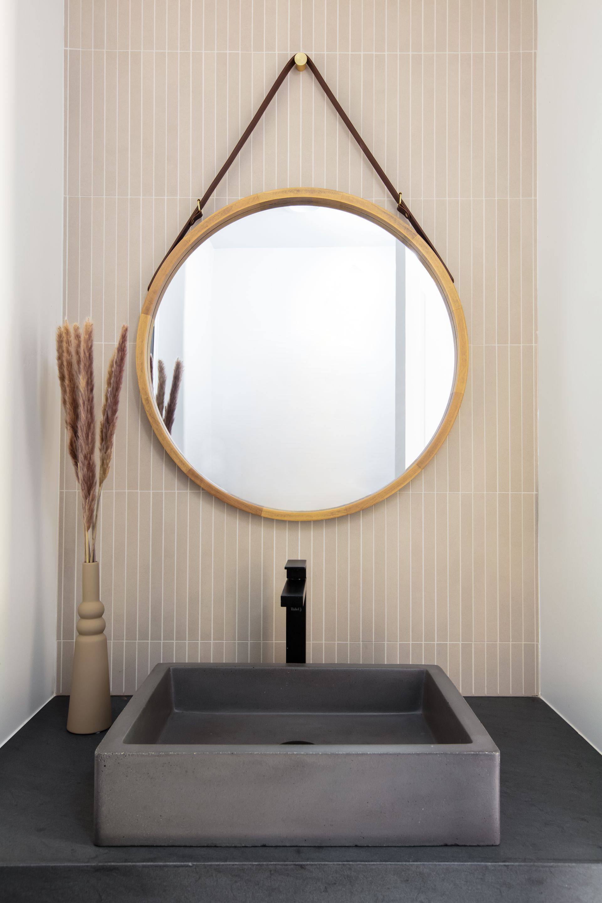 Modern bathroom vanity with round mirror, gray sink, black faucet, and woven wall decor.