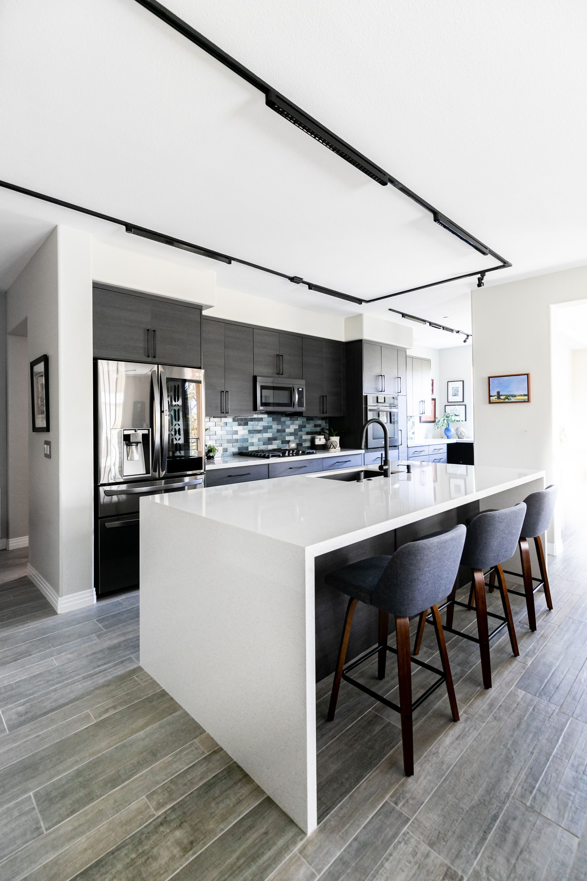 Modern kitchen with white island, black stools, gray cabinets, and wood-look flooring