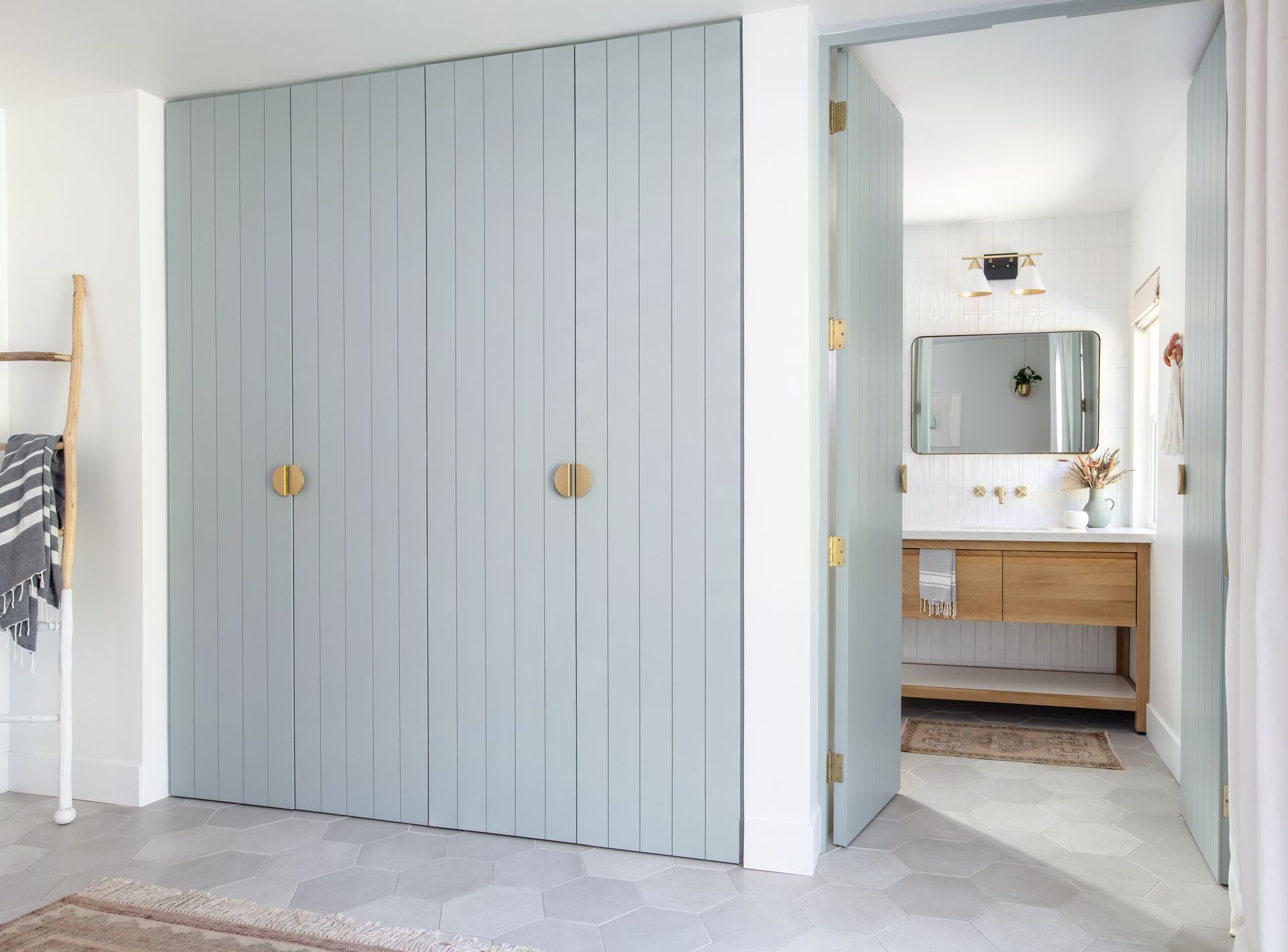 Light gray closet doors beside a bathroom vanity with a round mirror and gold fixtures.
