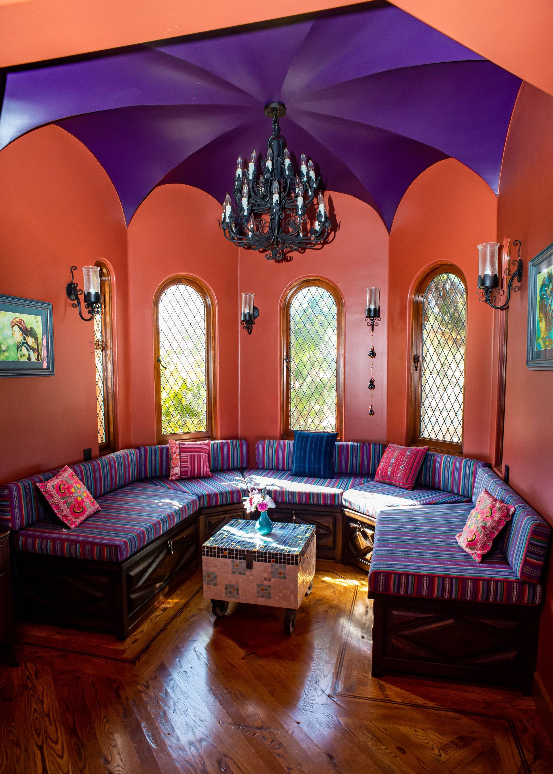 Colorful lounge with orange walls, purple ceiling, curved sectional seating, chandelier, and wood floor.