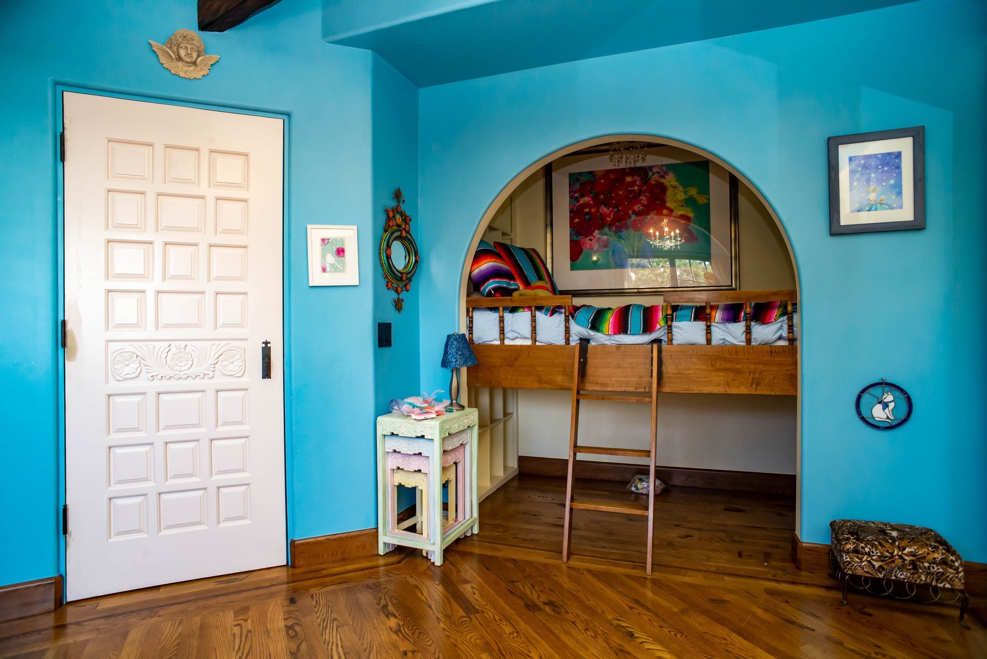 Bright blue room with white door, arched alcove shelves, and wooden floor with a small table.