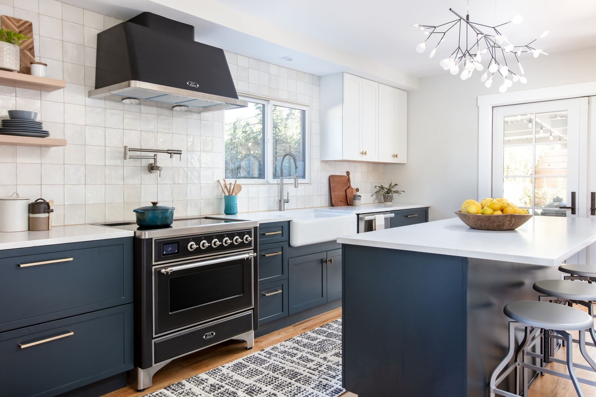 Bright modern kitchen with navy cabinets, black stove, white island, and bowl of fruit near a window.