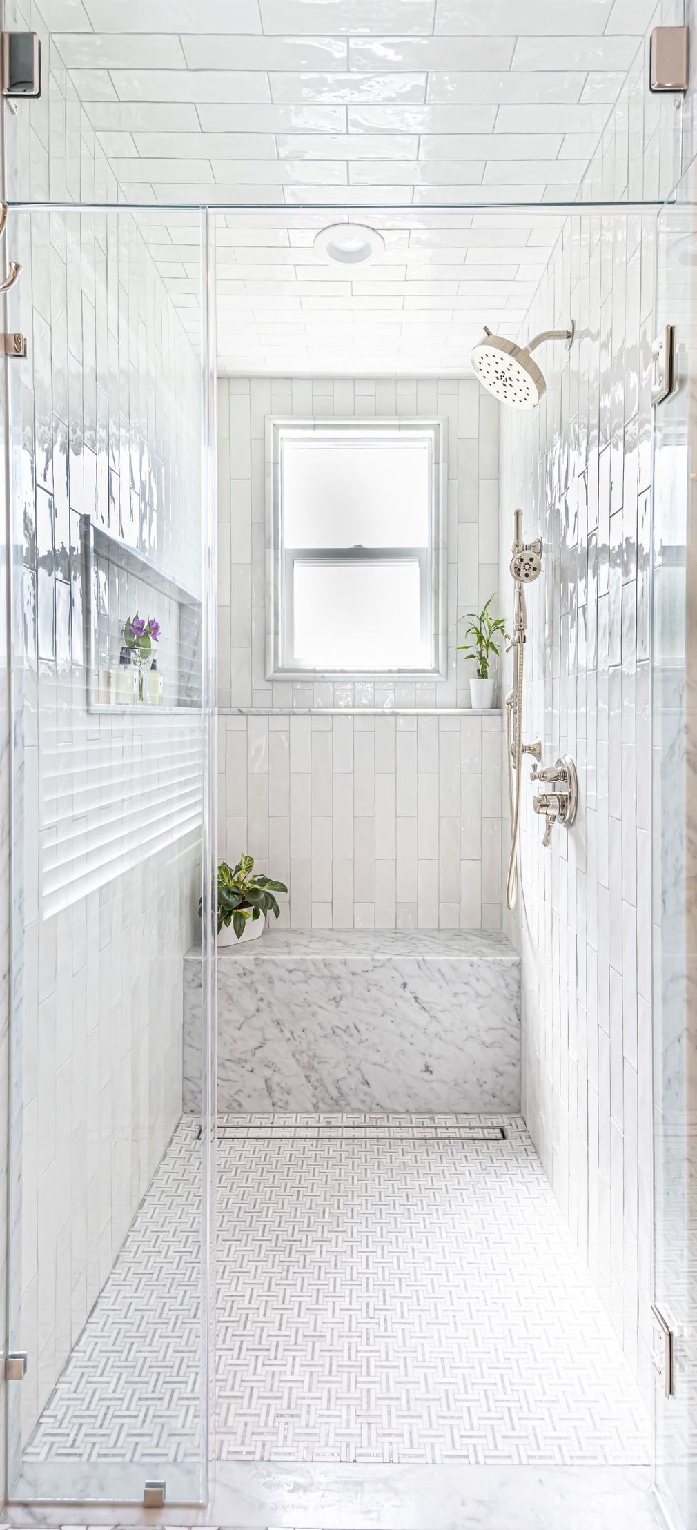 Bright white bathroom with paneled walls, mirror, and potted plants on a patterned floor