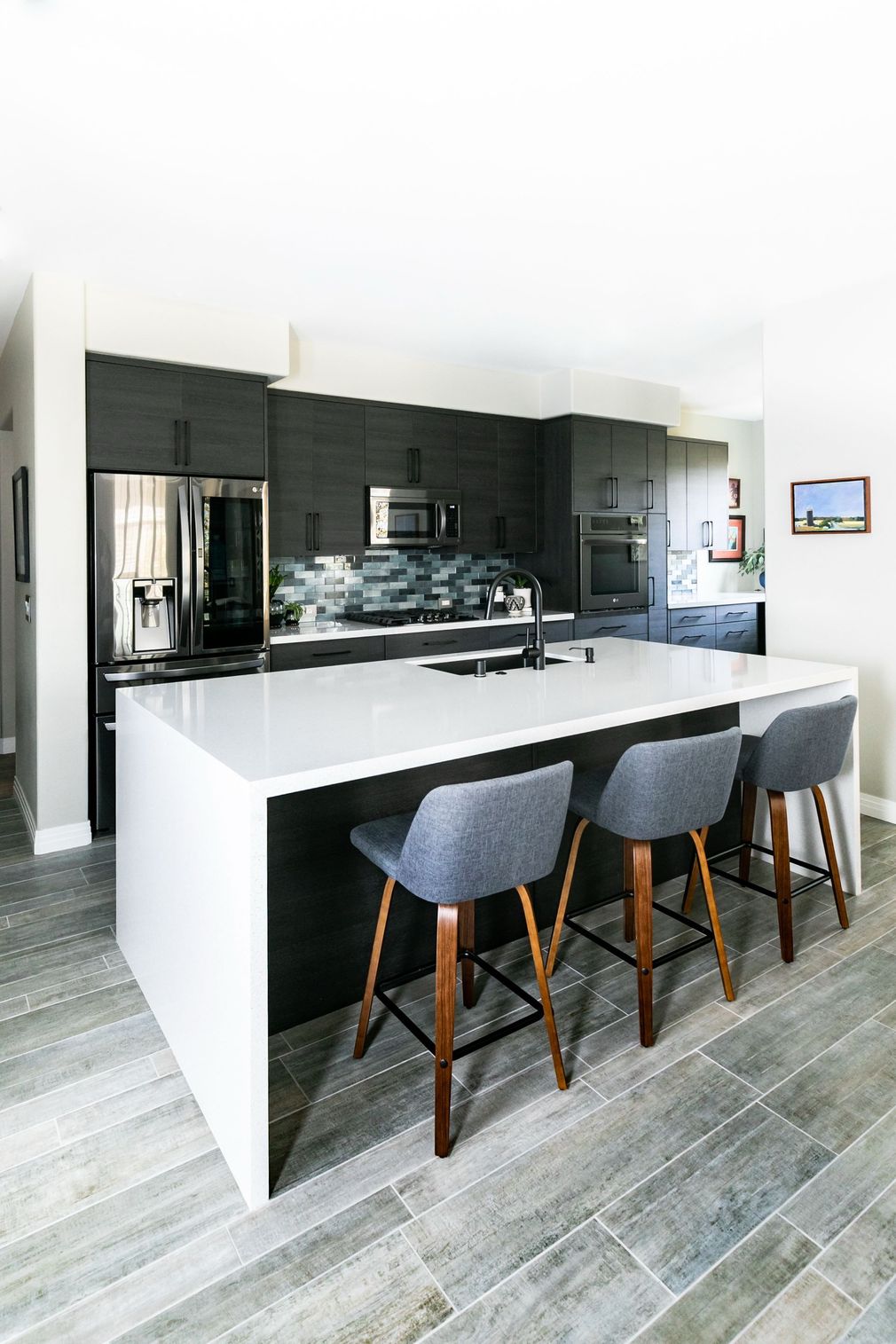 Modern kitchen with white island, gray bar stools, dark cabinets, and wood-look flooring