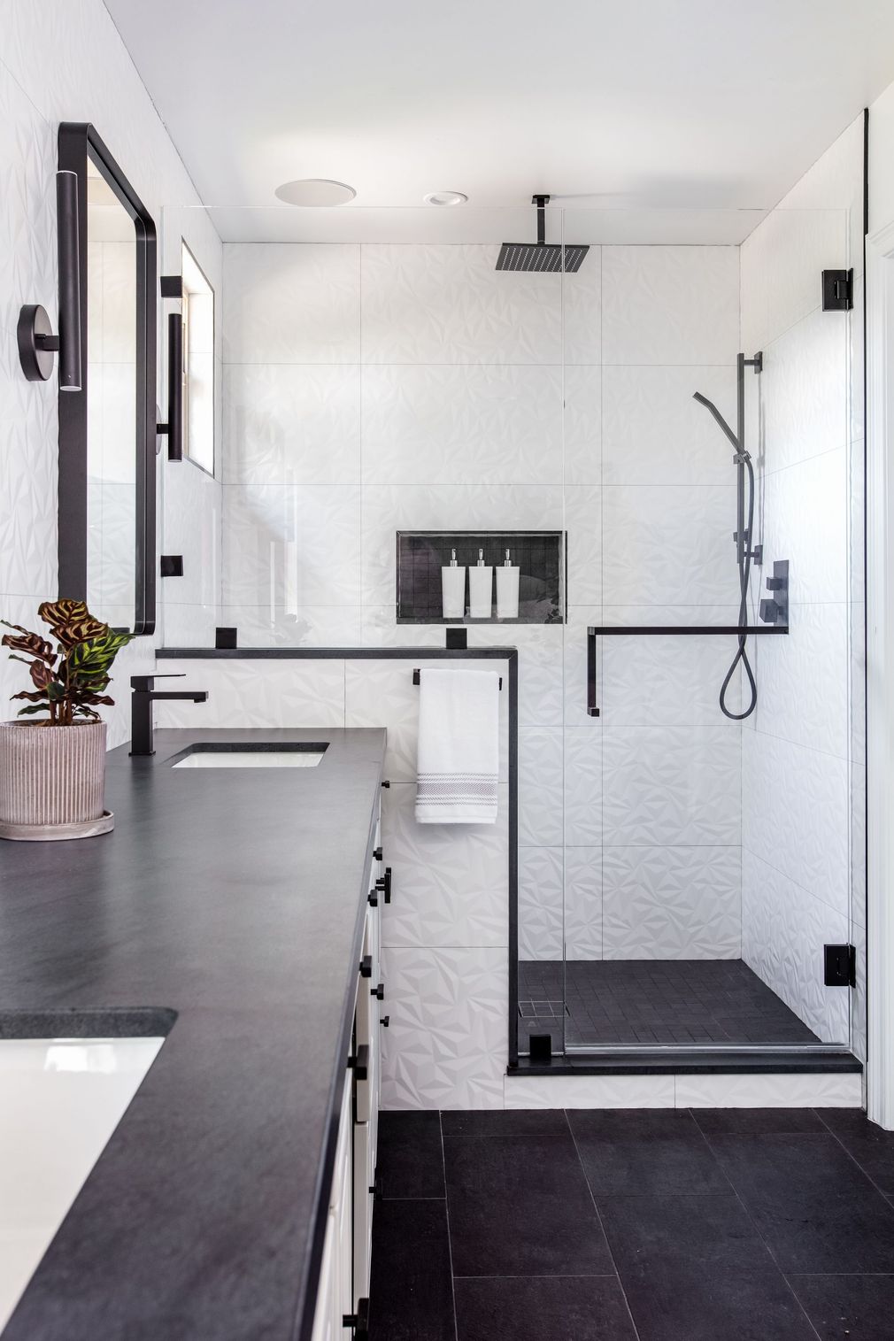 Modern white bathroom with black fixtures, walk-in shower, and dark countertop.