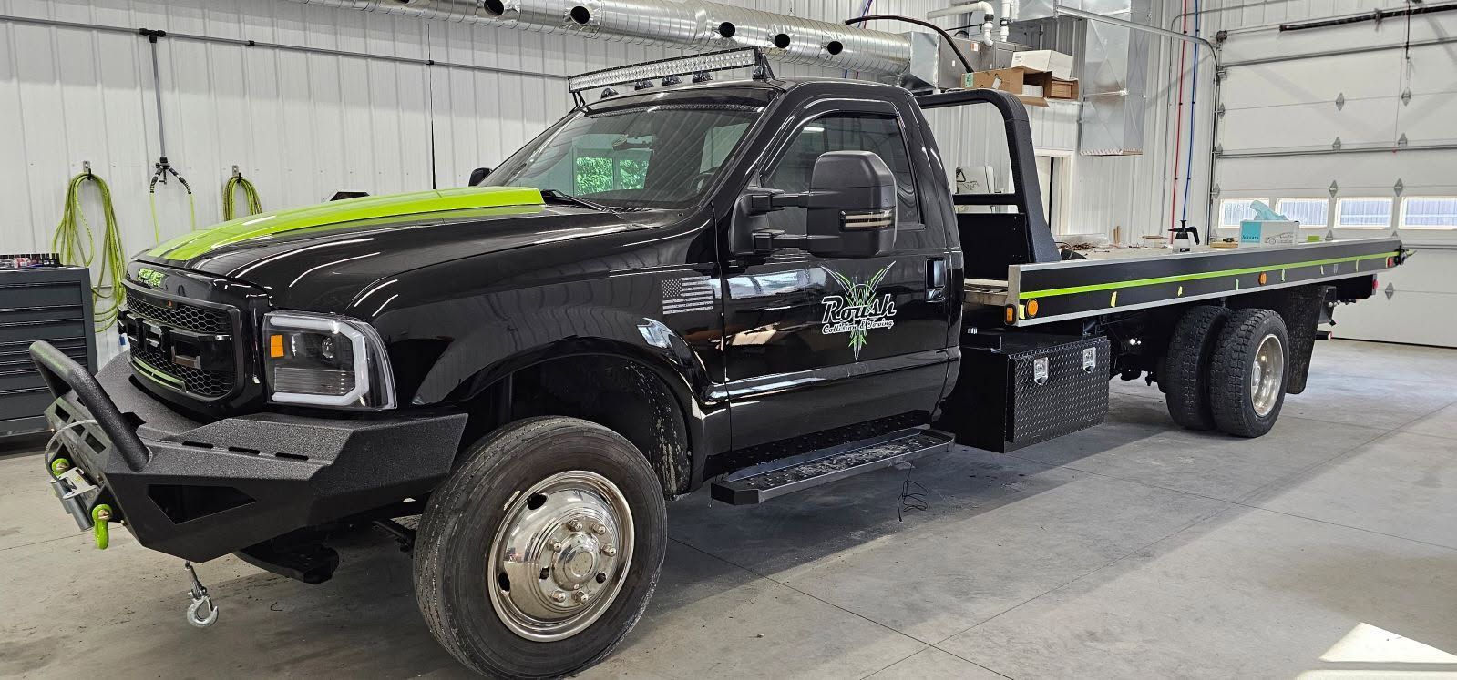 A black tow truck with a flat bed is parked in a garage.