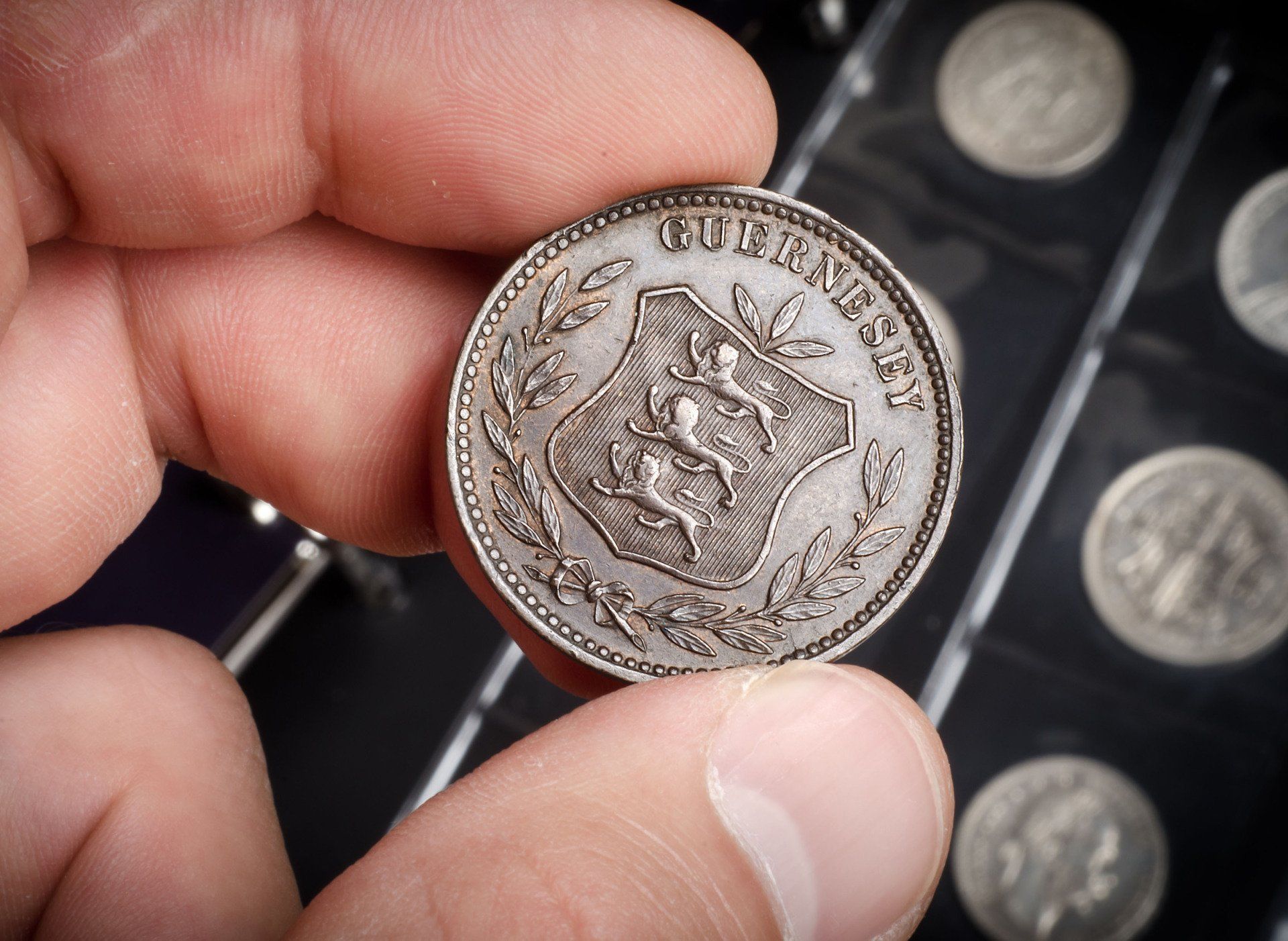 Hand holding an old silver coin with an emblem and the word 