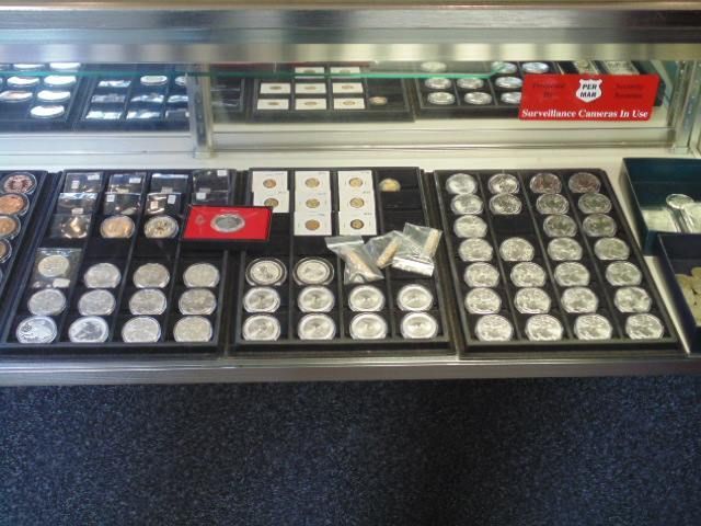 Display case with trays of coins, including silver rounds and other collectibles.