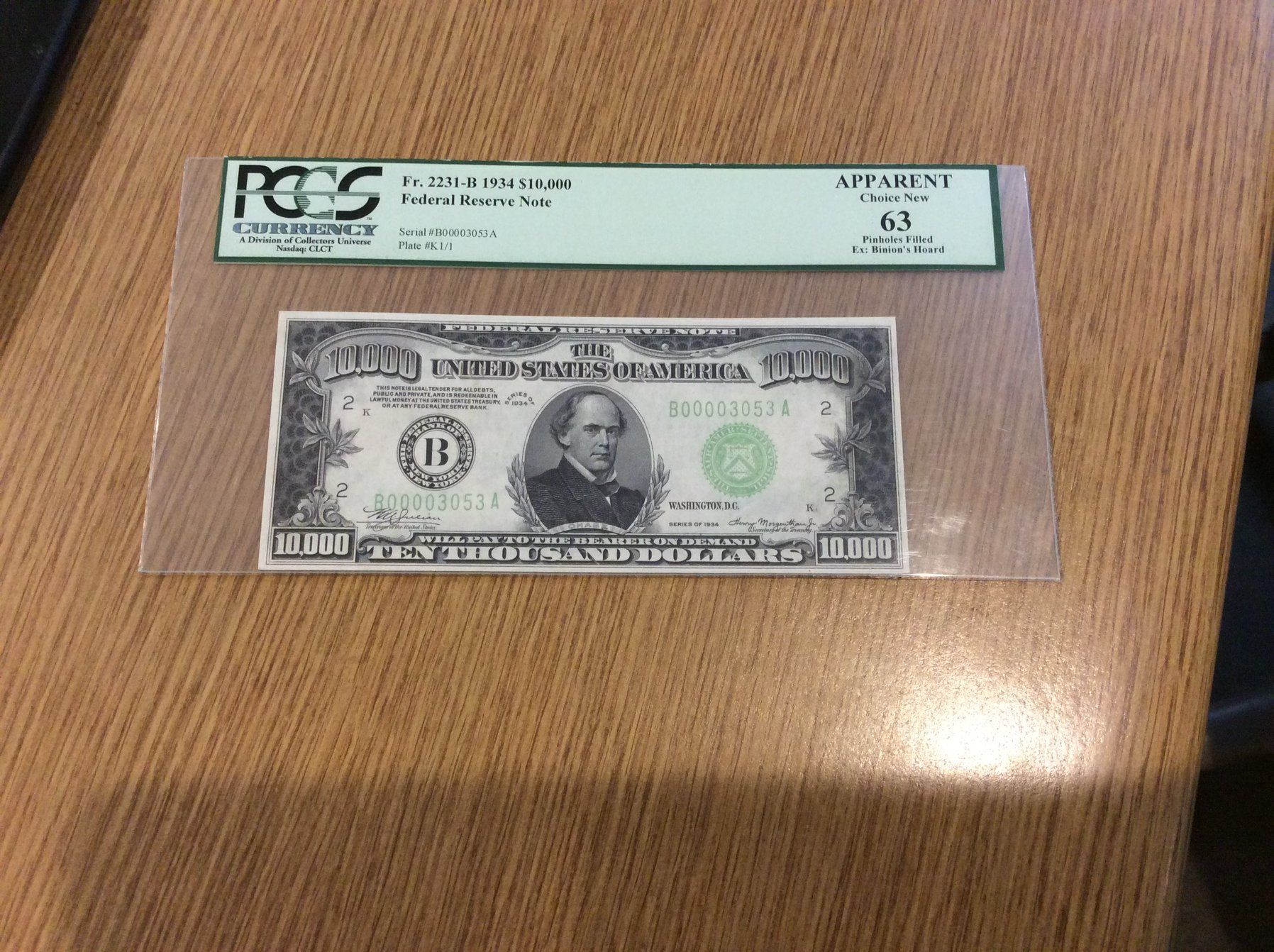 A $10 US bill, graded 63 by PCGS, in a clear protective holder on a wooden surface.