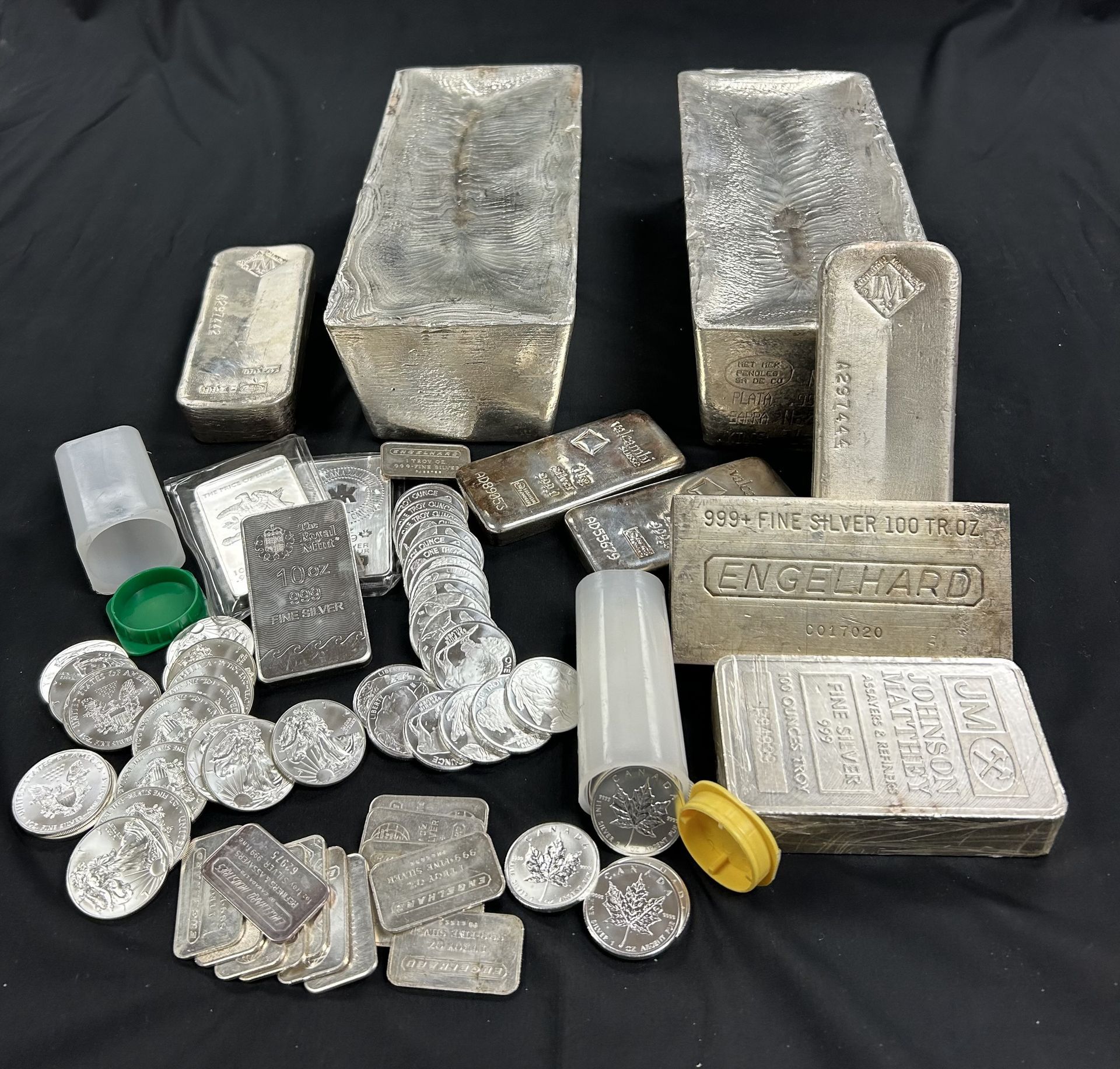 Pile of silver bars and coins, various shapes, on a black surface.