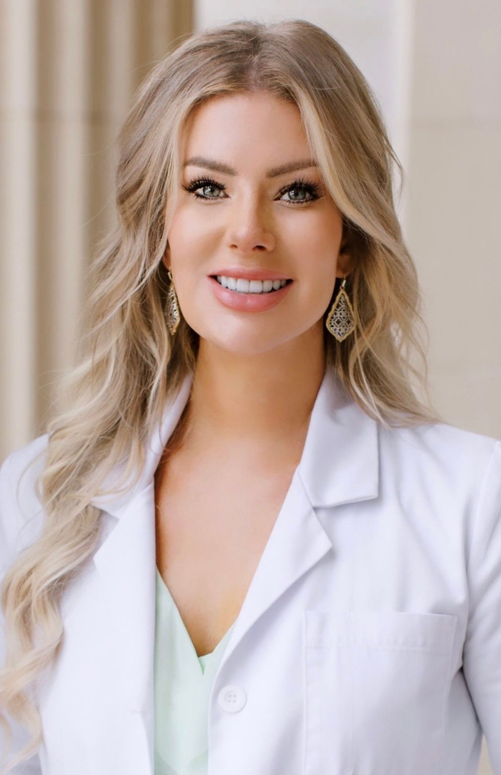 Christine Hedblom, RDH OMT in a white lab coat and earrings is smiling for the camera.