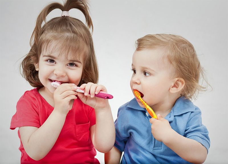 A boy and a girl are brushing their teeth together.