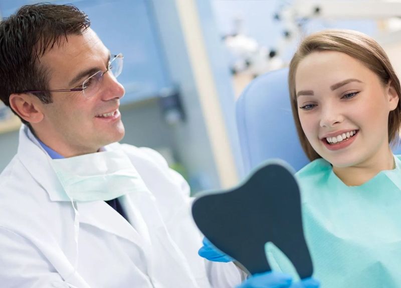 A dentist is looking at a patient 's teeth in a mirror.