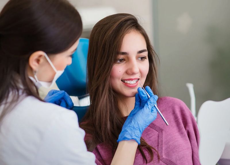 A woman is sitting in a dental chair while a dentist examines her teeth.