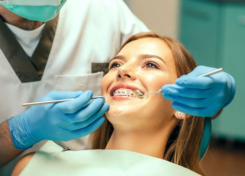 A woman is sitting in a dental chair while a dentist examines her teeth.