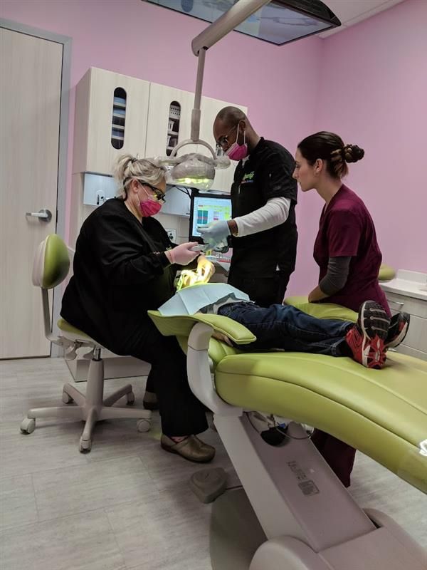 A woman is sitting in a dental chair talking to two dentists.
